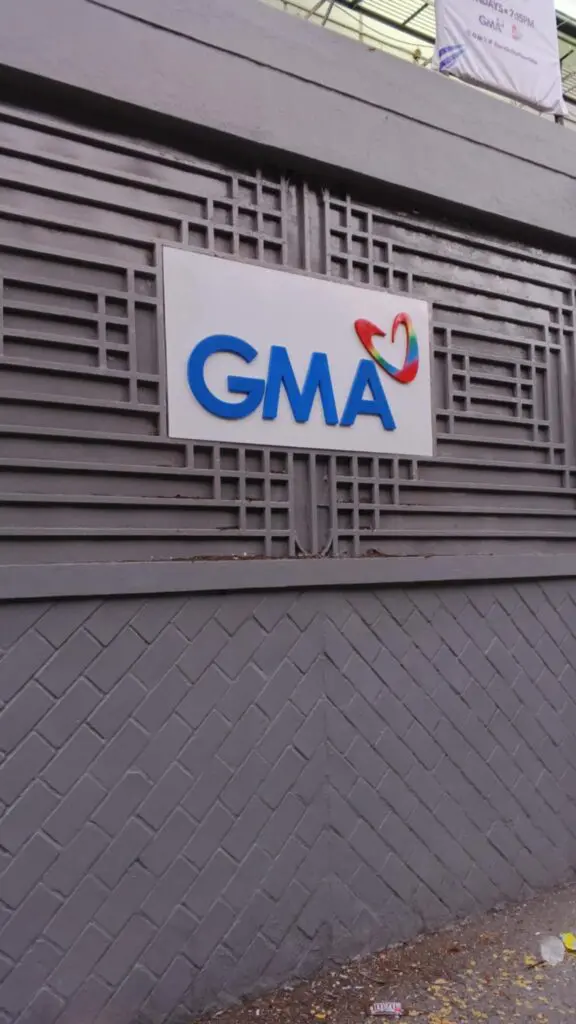 Acrylic building signage with blue GMA letters and colorful heart, geometric gray wall, Metro Manila sign maker Philippines by M&G Global Ads.