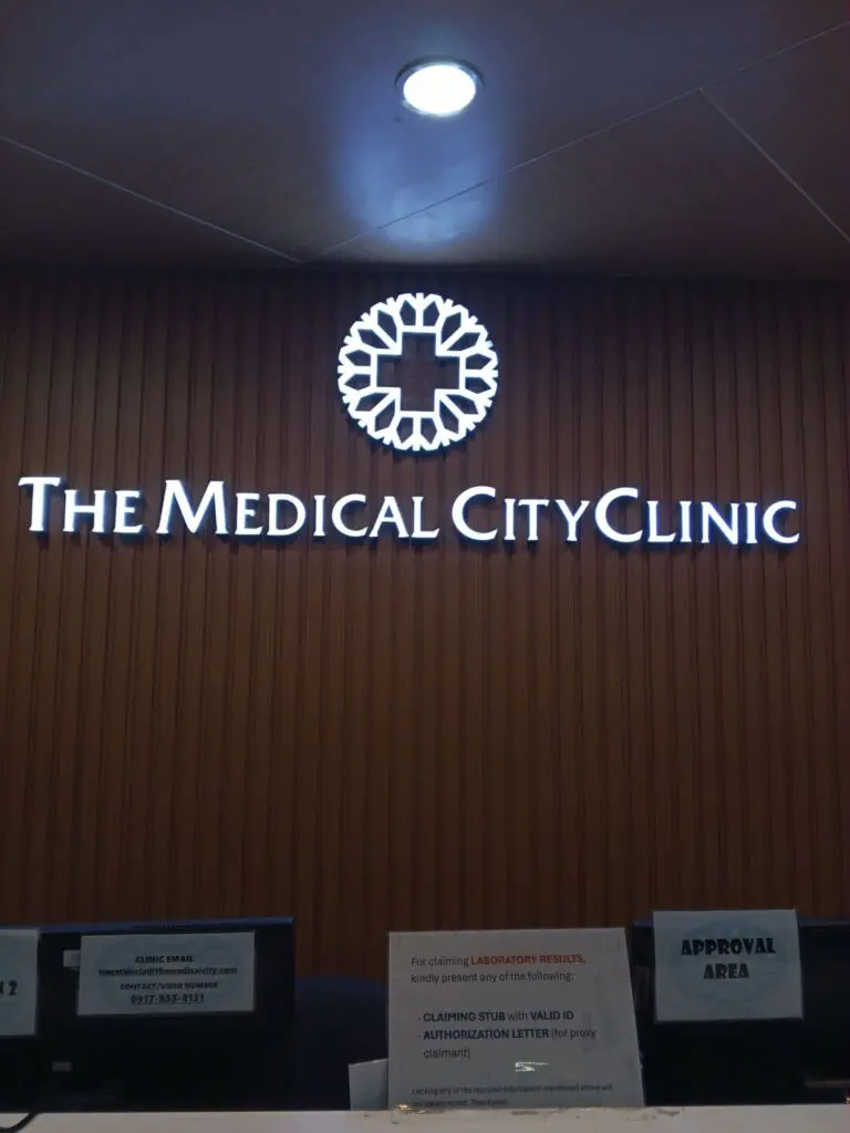 Indoor acrylic LED signage for The Medical City Clinic featuring a glowing logo and circular cross design above the reception desks, with acrylic wayfinding and information signs for APPROVAL AREA and laboratory results; sign maker Philippines, Metro Manila. Signage by M&G Global Ads.