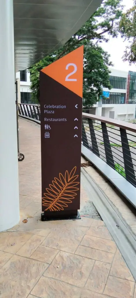 Indoor wayfinding sign, likely acrylic, on the second floor pointing to Celebration Plaza and restaurants with restroom icons below; features black and orange colors with a leaf design, installed beside a railing and walkway in Metro Manila. Sign maker Philippines by M&G Global Ads.