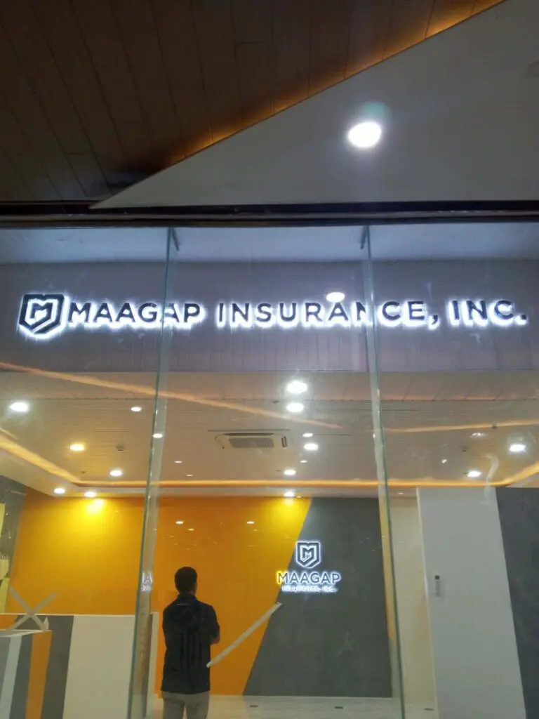 A person stands in front of a glass-walled office with an indoor, brightly lit LED acrylic signage that reads MAAGAP INSURANCE, INC., inside a modern yellow and gray interior. Sign maker Philippines for Maagap Insurance, Metro Manila by M&G Global Ads.