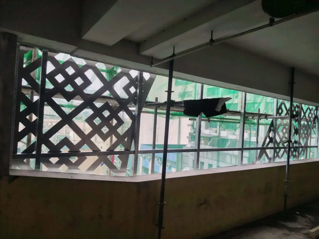 Building signage installation in progress at a partially constructed building in Metro Manila, featuring lattice-patterned window grids, green safety netting, and exterior scaffolding. The unfinished interior includes a piece of black cloth hanging on the railing. Sign maker Philippines by M&G Global Ads.