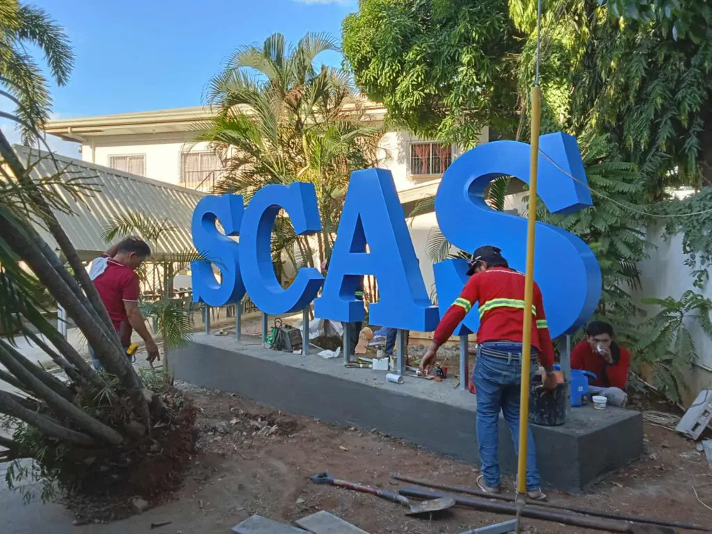 Outdoor acrylic building signage installation for SCAS with blue letters on concrete base, Metro Manila, sign maker Philippines by M&G Global Ads.