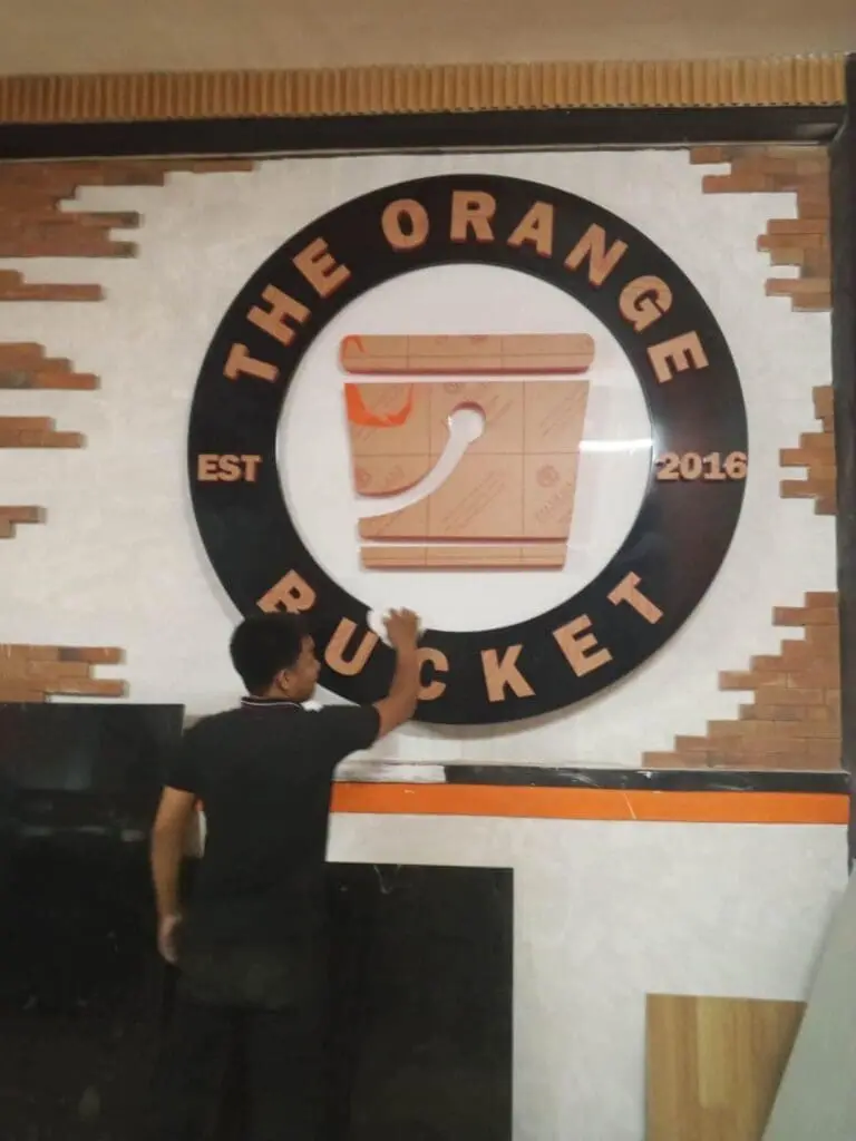 Stainless steel building signage for The Orange Bucket, circular sign on brick and white wall in Metro Manila by sign maker Philippines M&G Global Ads.