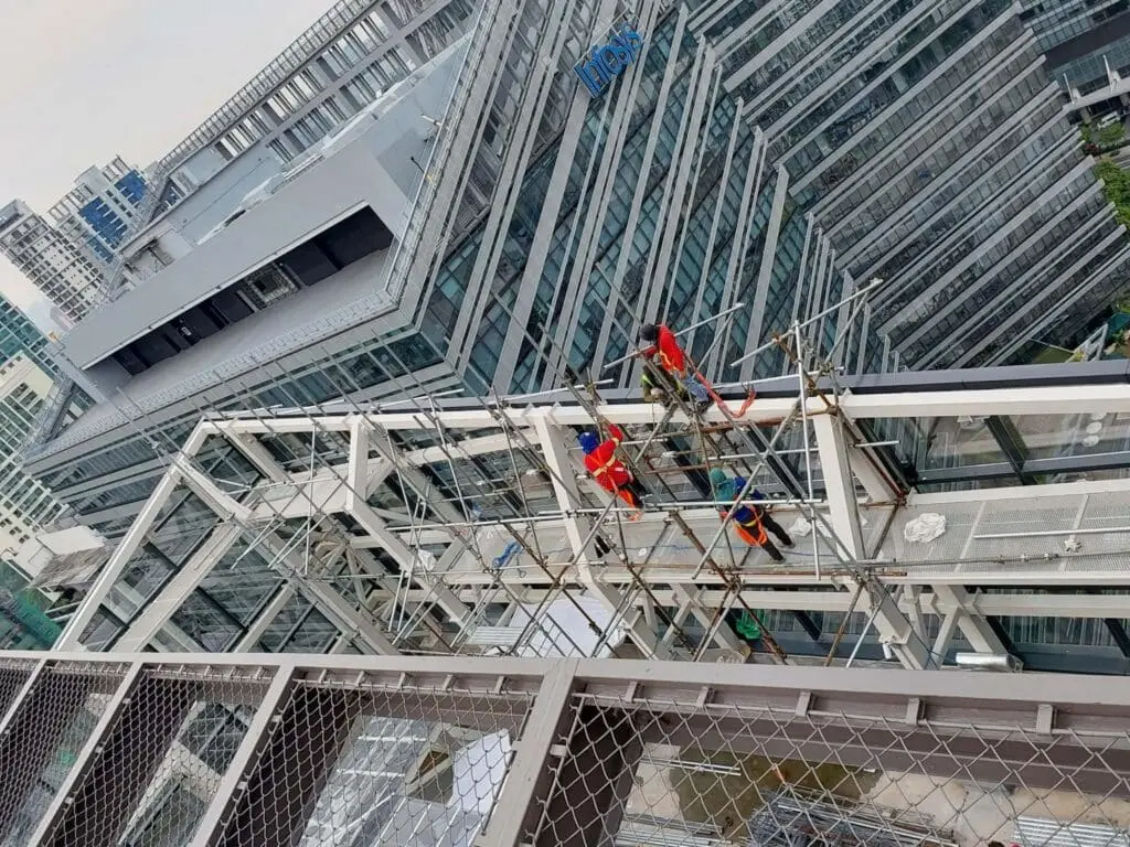 Three workers install outdoor building signage on glass office in Metro Manila cityscape, sign maker Philippines by M&G Global Ads.