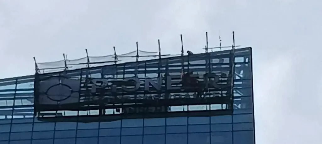 Sign maker Philippines installing outdoor building signage on glass facade, Metro Manila. Overcast sky. By M&G Global Ads.