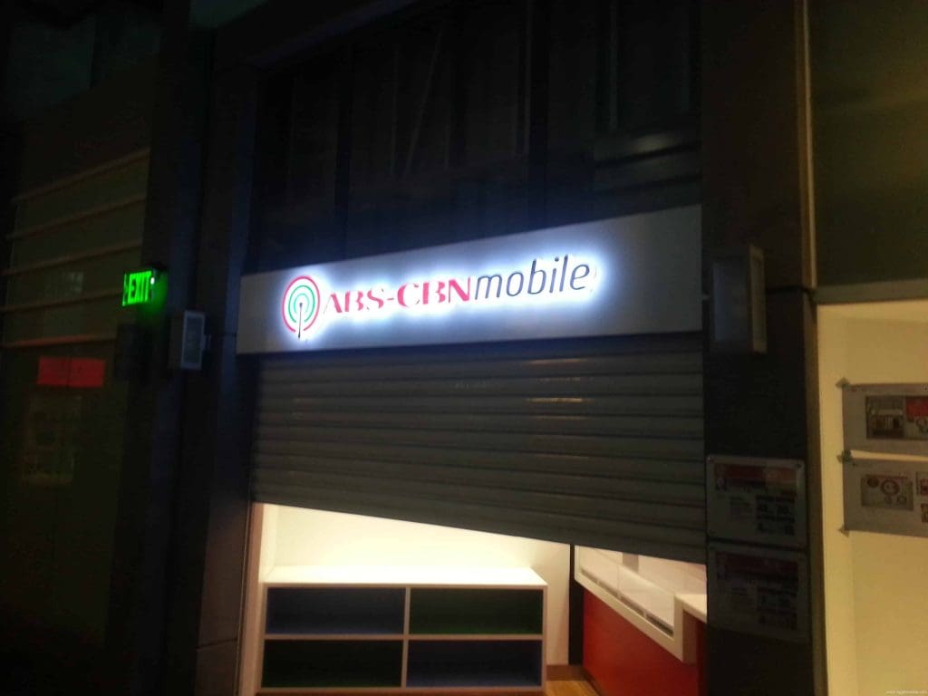 ABS-CBNmobile LED signage above a store with partially closed shutter in Quezon City, dimly visible interior, by M&G Global Ads.