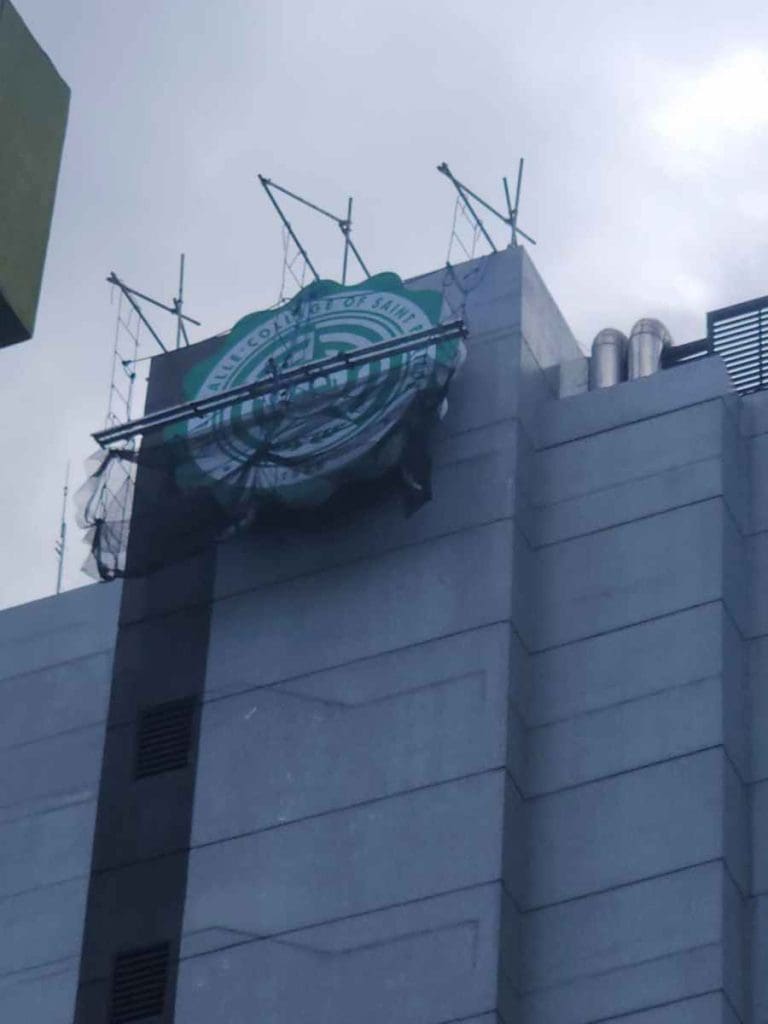 Damaged Starbucks Coffee outdoor signage on tall gray building in Makati with exposed metal supports. by M&G Global Ads.
