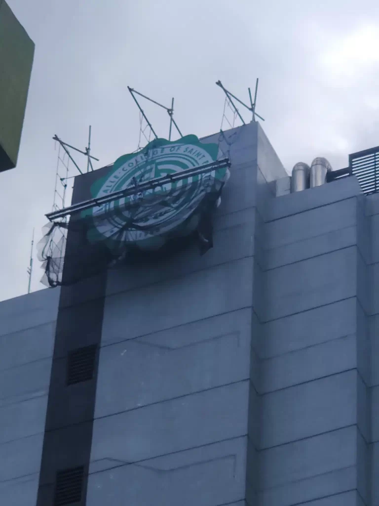 Damaged circular billboard signage with scaffolding on gray building in Ortigas, net hanging below, cloudy sky. By M&G Global Ads.