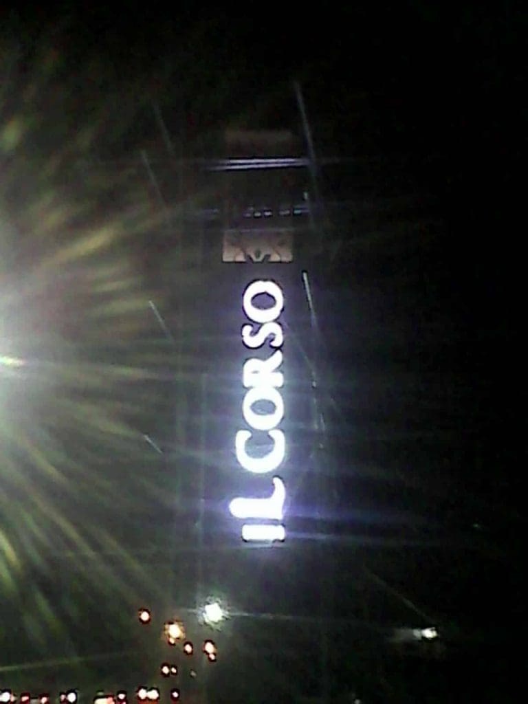 Vertical white neon signage for IL CORSO on a tall tower at night in BGC, with light flares, by M&G Global Ads.