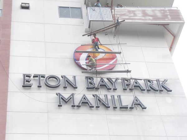 Building signage installation for Eton Baypark Manila in Makati, workers on scaffold mounting round sign by M&G Global Ads.