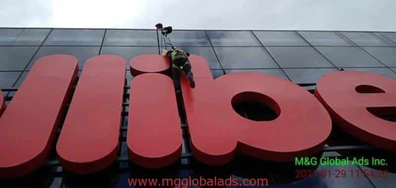 Worker cleaning 3D building signage letters on glass exterior in Makati, Philippines by M&G Global Ads.