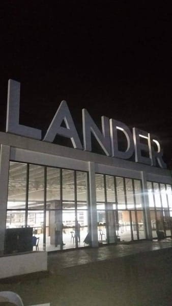 LANDER illuminated acrylic signage on modern glass building at night in BGC, interior lights visible. By M&G Global Ads.