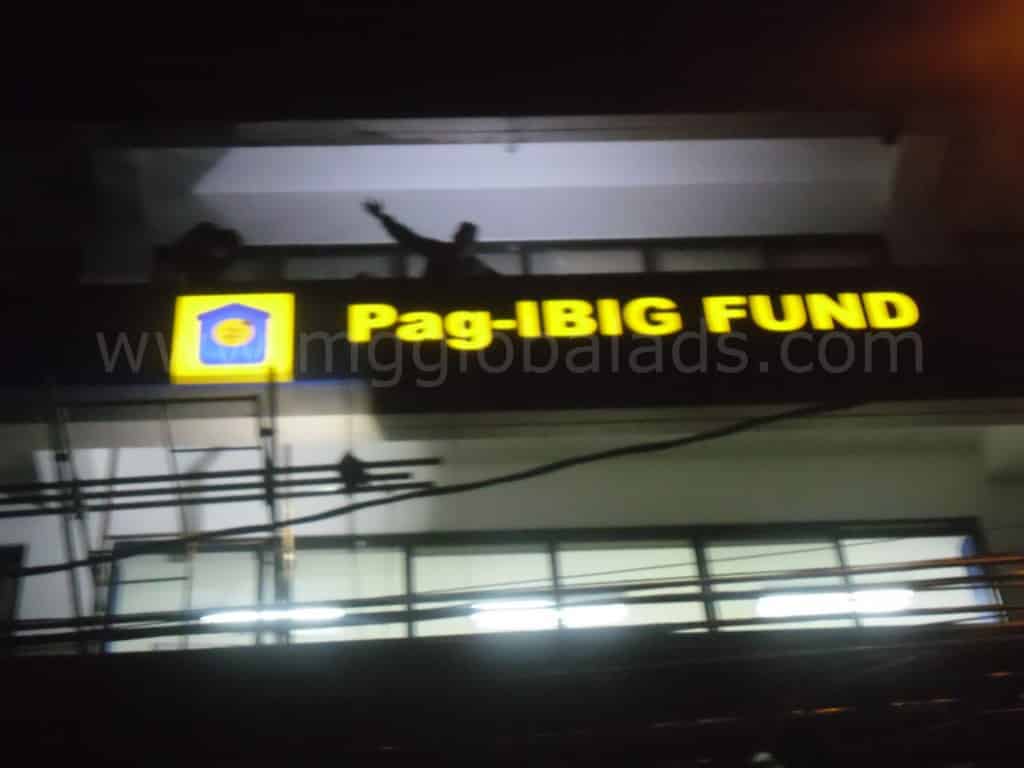 Pag-IBIG Fund LED building signage glowing at night in Metro Manila, with people on the balcony above, by M&G Global Ads.