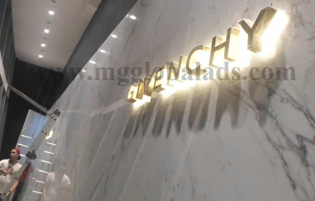 LED signage for GIVENCHY on a marble wall in Makati with gold illuminated letters, people, and ladder by M&G Global Ads.