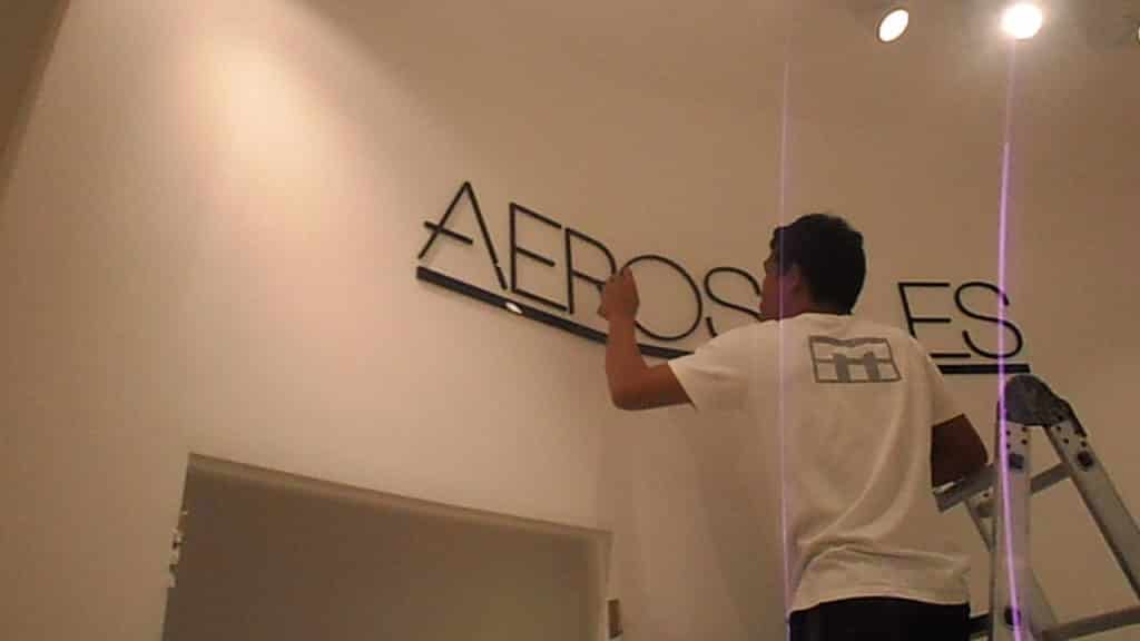 Installing black acrylic AEROS signage on white wall in Makati, under spotlights, by M&G Global Ads.