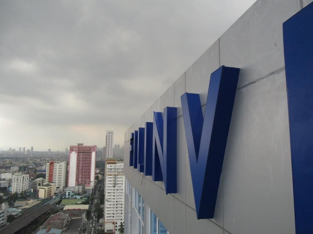 Large blue LED billboard signage on tall building in Makati cityscape under overcast sky, by M&G Global Ads.