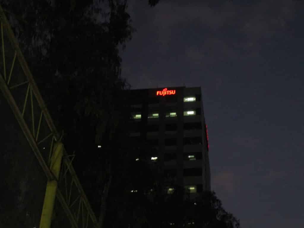 Fujitsu acrylic signage on dark office building at night in Makati, illuminated windows, by M&G Global Ads.