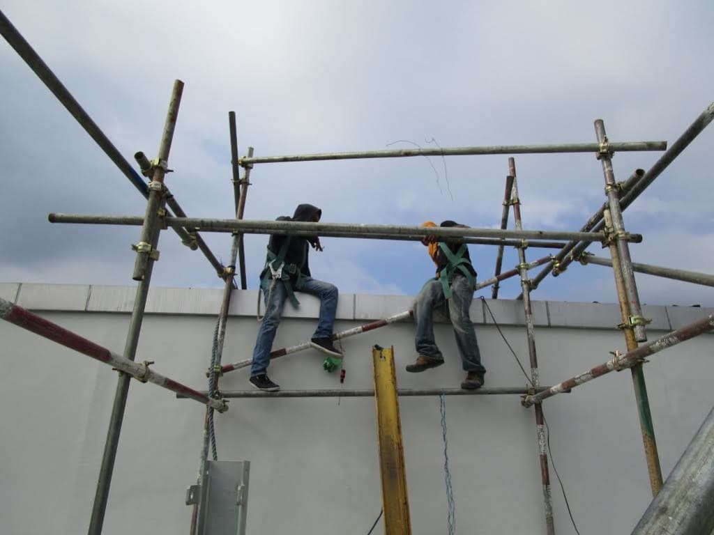 Acrylic signage installation in BGC: two harnessed workers on scaffolding, one climbing, one handling tools by M&G Global Ads.
