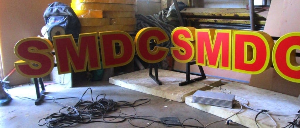 SMDC acrylic indoor signage at a busy workshop in Makati, surrounded by tools and materials, by M&G Global Ads.