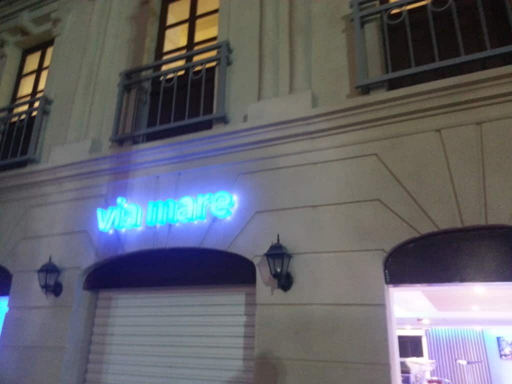 Neon blue LED signage for Via Mare restaurant above a closed white shutter at night in Makati, by M&G Global Ads.