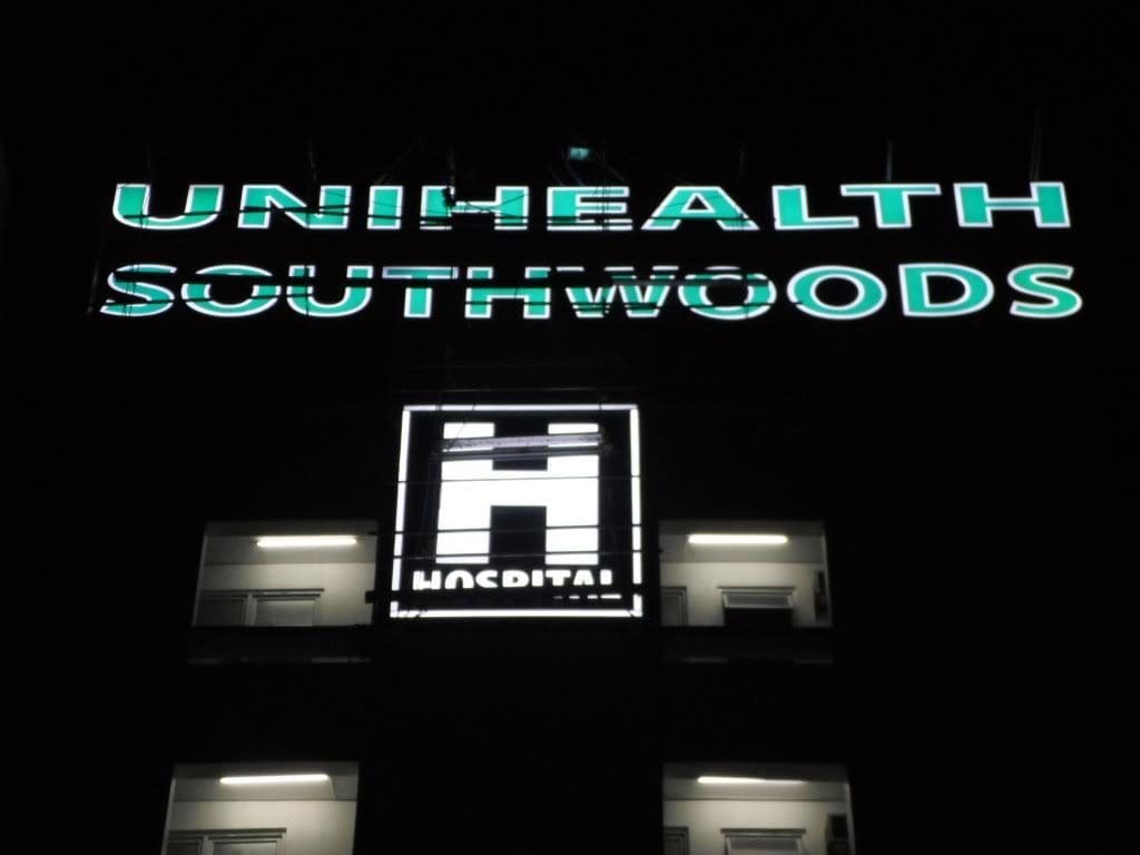 Acrylic signage for UNIHEALTH SOUTHWOODS being cleaned by workers on tall building, Makati location, by M&G Global Ads.