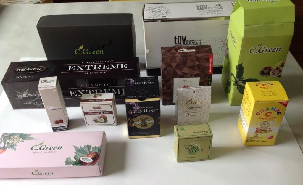 Assorted boxed products beside custom acrylic signage, displayed for a Quezon City client. Product packaging in many colors by M&G Global Ads.
