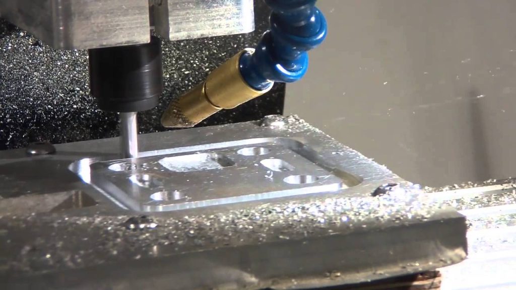 CNC milling for indoor signage fabrication in Makati—precision metal parts, blue coolant nozzle, shavings by M&G Global Ads.