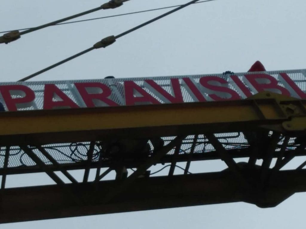 Outdoor billboard signage with red PARAVISI letters on white, metal frame, cloudy sky, in Makati by M&G Global Ads.