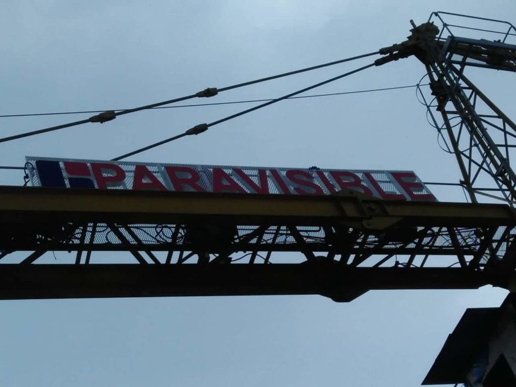 Billboard signage for PARAVISIBLE held by crane in Makati, blue and red design on side, by M&G Global Ads.