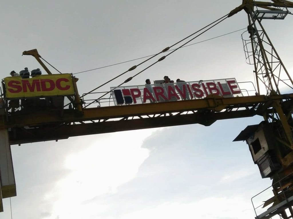 Outdoor crane signage for SMDC and PARAVISIBLE in Makati with banners, cloudy sky view by M&G Global Ads.