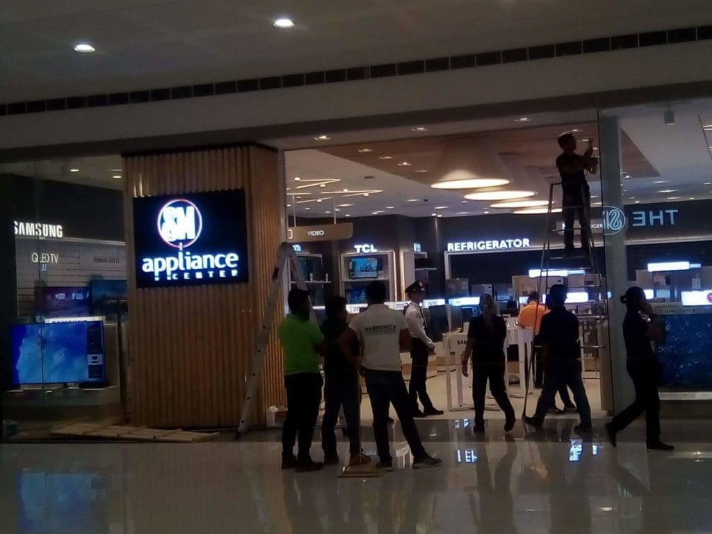 SM Appliance Center indoor signage installation in Quezon City mall entrance with workers and appliances, by M&G Global Ads.