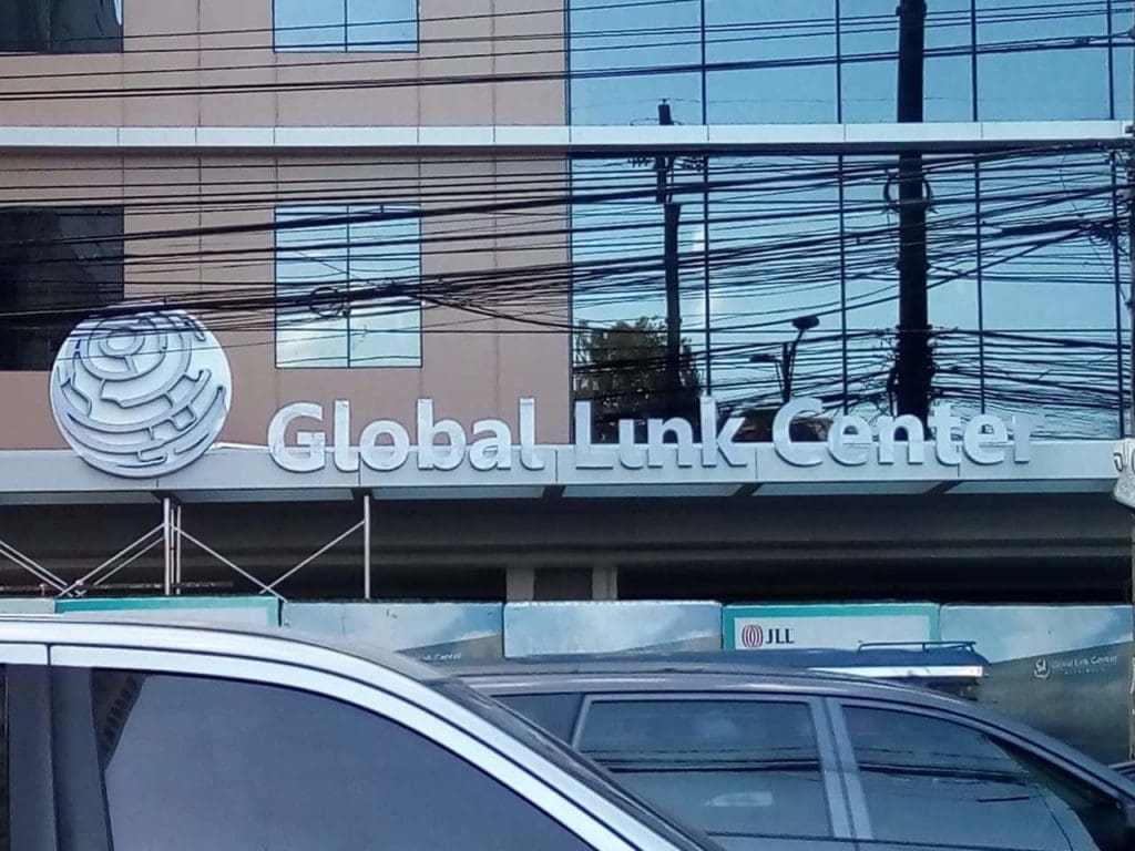 Metallic building signage for Global Link Center with globe logo, seen in Ortigas, cars parked in front. By M&G Global Ads.