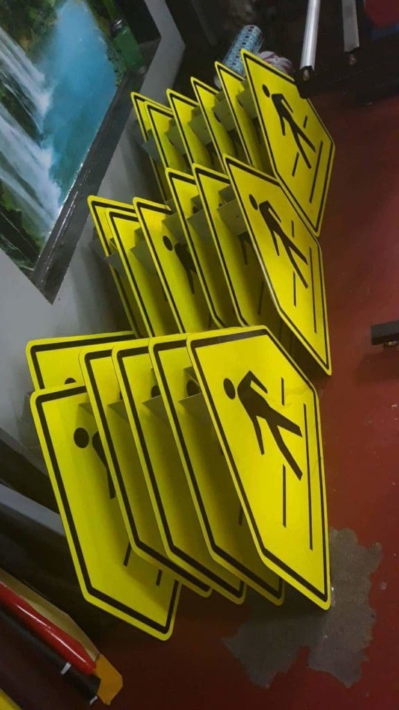 Pedestrian crossing outdoor signage stacked on a red floor in Makati, yellow signs with black figures by M&G Global Ads.