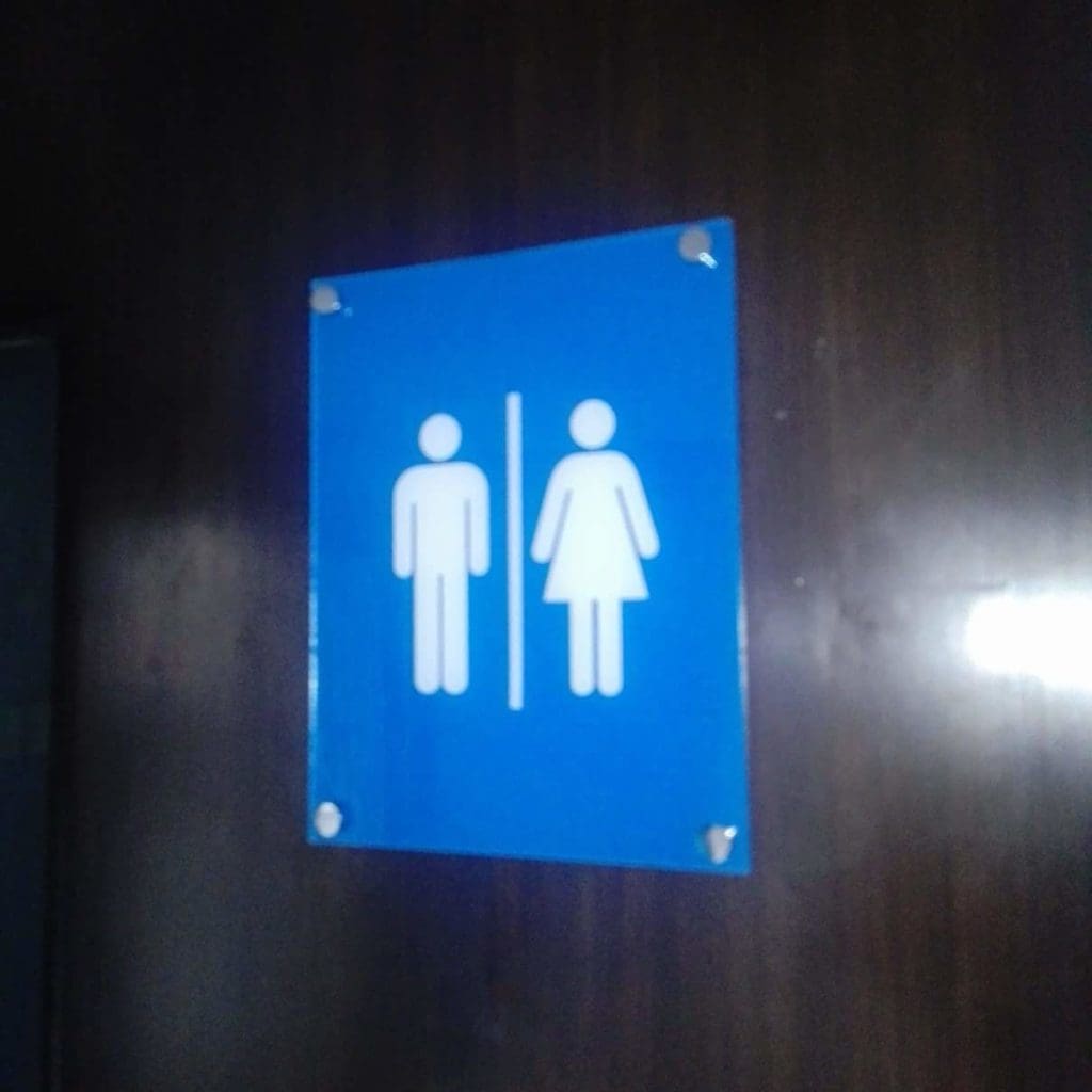 Restroom sign, blue metallic with man and woman icons, on a dark wall in Quezon City by M&G Global Ads.