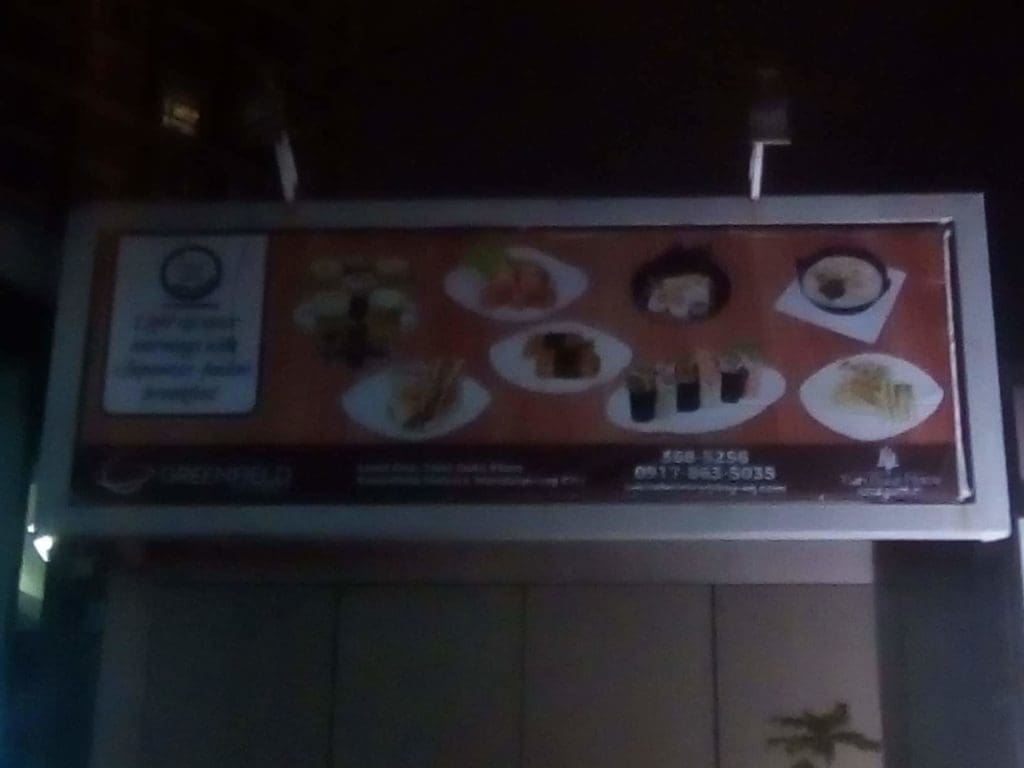 Blurry billboard signage for Japanese restaurant with sushi plates at night in Makati, text unreadable, by M&G Global Ads.