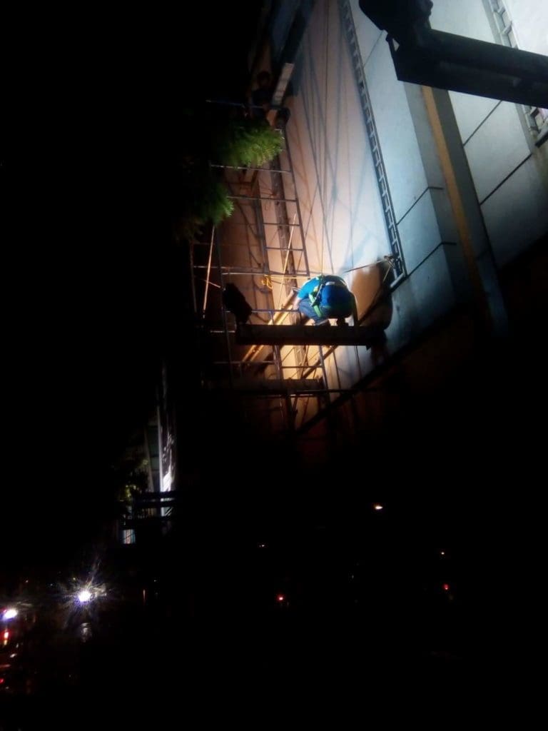 Worker installs illuminated building signage at night on scaffolding in Makati, minimal details visible. By M&G Global Ads.