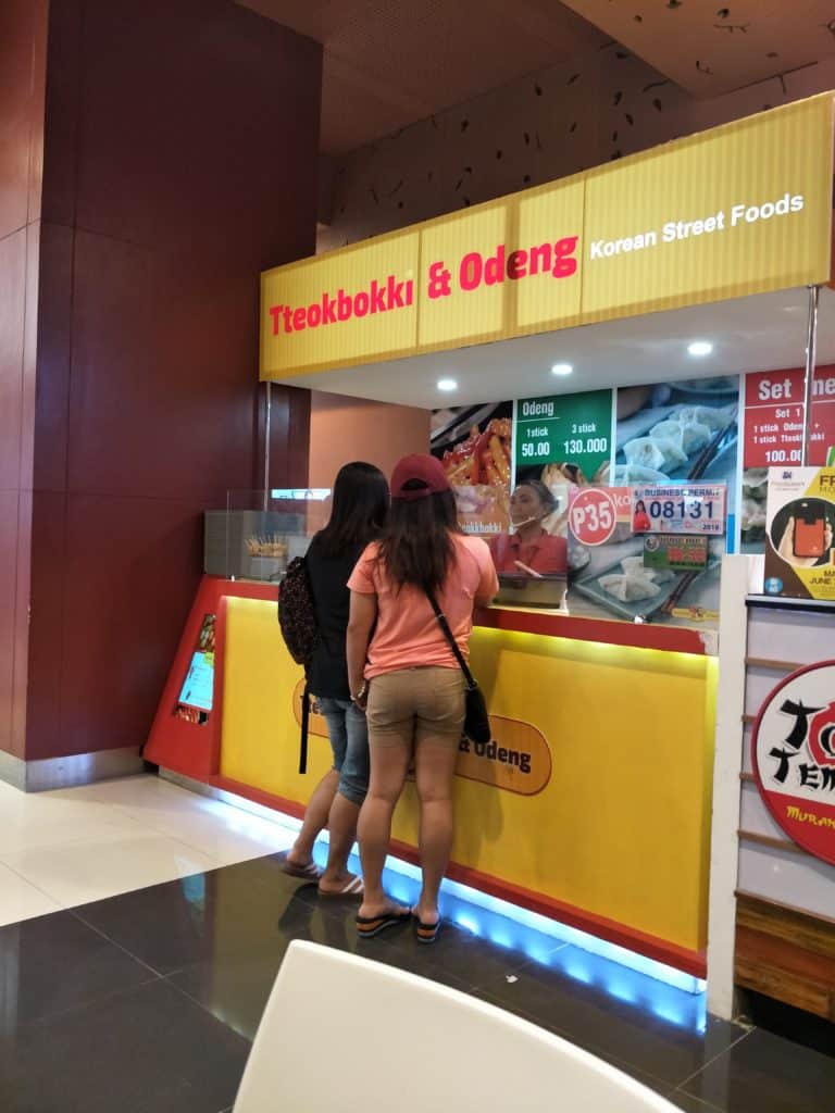 Two women at a Tteokbokki & Odeng stall with yellow and red LED signage in Quezon City by M&G Global Ads.