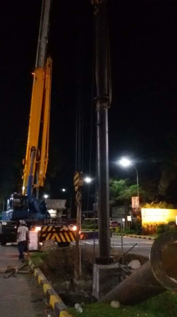 Billboard installation in Makati at night with a yellow crane lifting a metal pole and workers onsite, by M&G Global Ads.