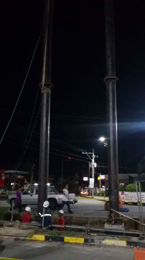 Construction workers by billboard sign in Mandaluyong at night, pickup truck parked nearby, streetlights glowing by M&G Global Ads.