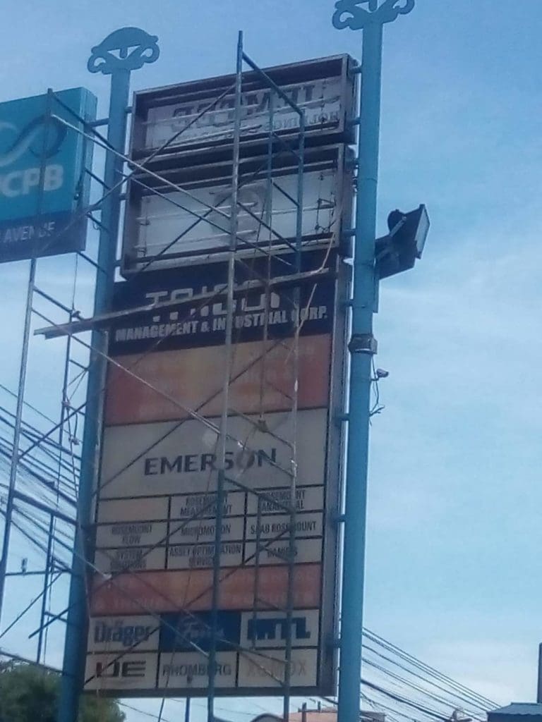 Pylon signage with multiple business names and scaffolding in Ortigas, blue sky and power lines. By M&G Global Ads.