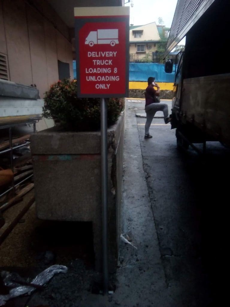 Red acrylic Delivery Truck Loading & Unloading Only signage beside a planter in Makati alley, by M&G Global Ads.
