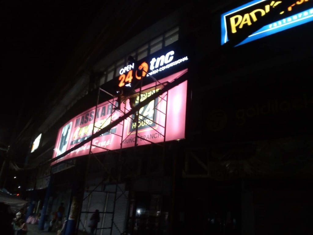 Open 24 TNC metallic storefront sign installation in Makati at night with illuminated signage by M&G Global Ads.