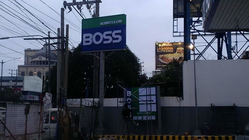 Outdoor signage for BOSS in bold white on blue, near power lines and billboards in Ortigas, by M&G Global Ads.