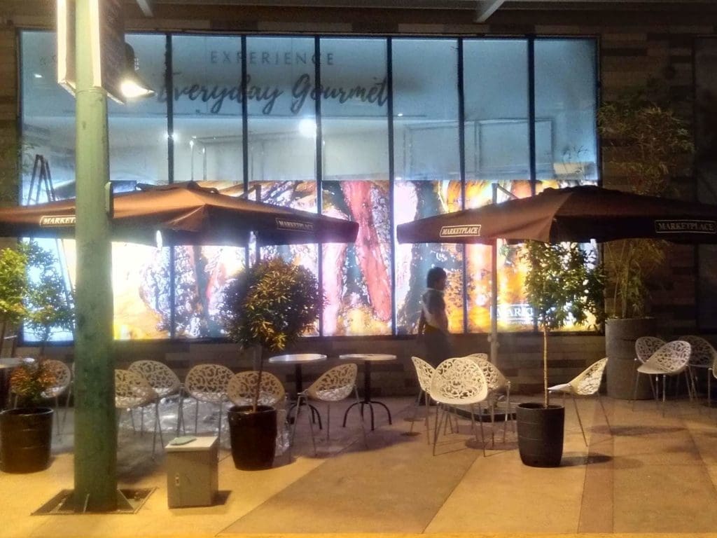 Outdoor restaurant with empty white tables, bright lightbox signage, grilled meat window graphics in BGC by M&G Global Ads.