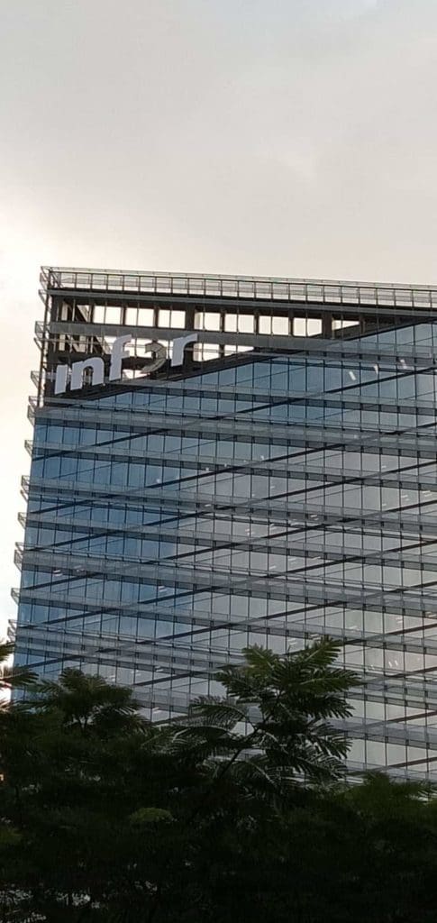 Infor illuminated building signage on a modern glass office in BGC, Metro Manila, with green trees and cloudy sky by M&G Global Ads.