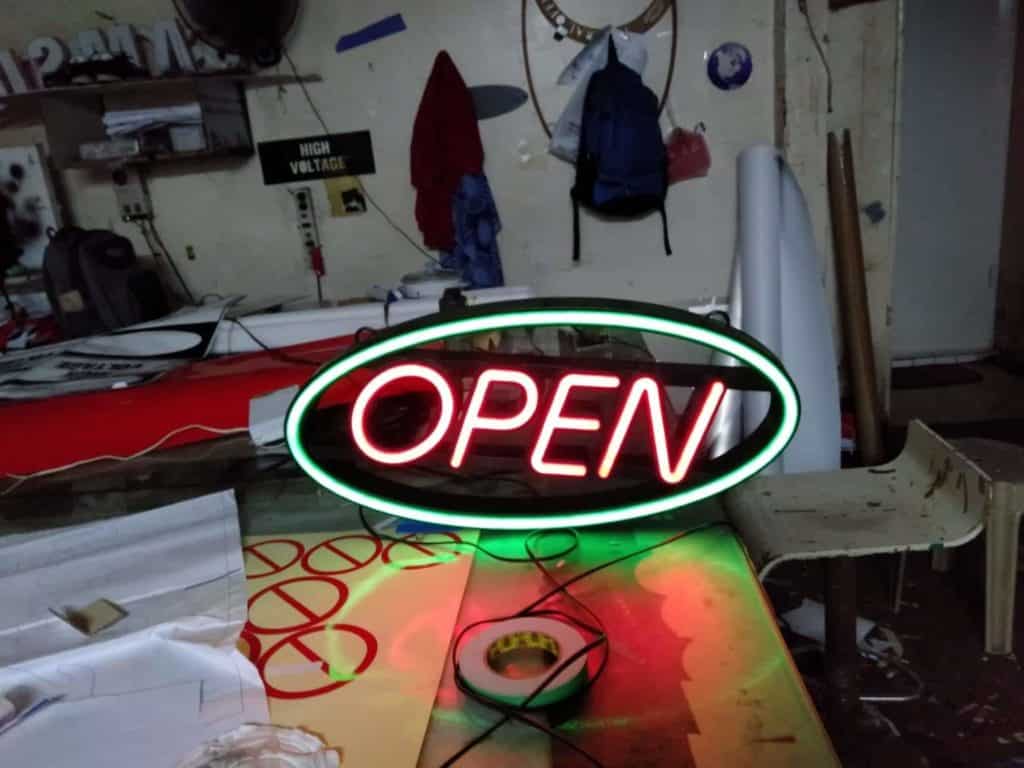 Neon acrylic OPEN signage in bright red with green oval, displayed on a table in Makati, by M&G Global Ads.