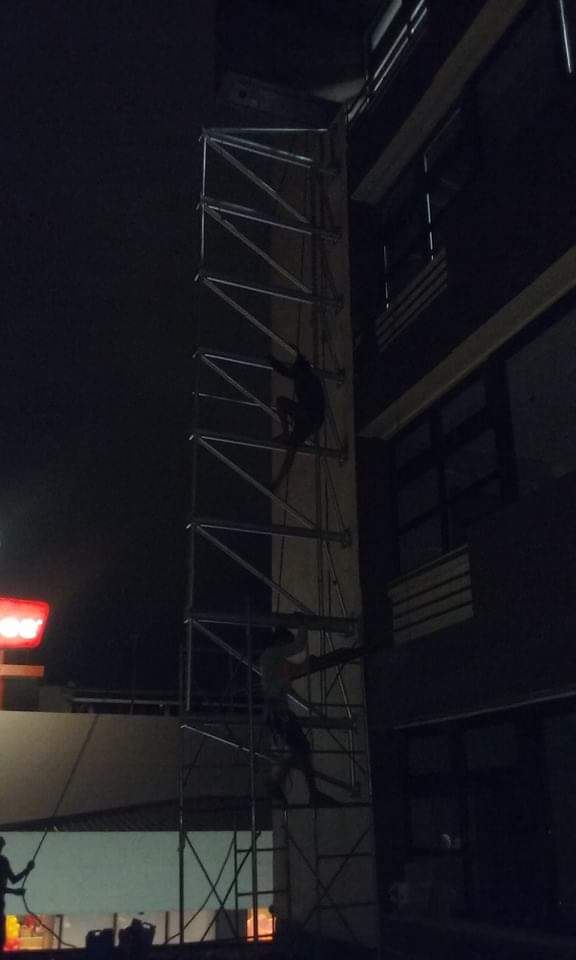 Two people install billboard signage on metal scaffolding at night beside a building in Makati, silhouettes visible. by M&G Global Ads.