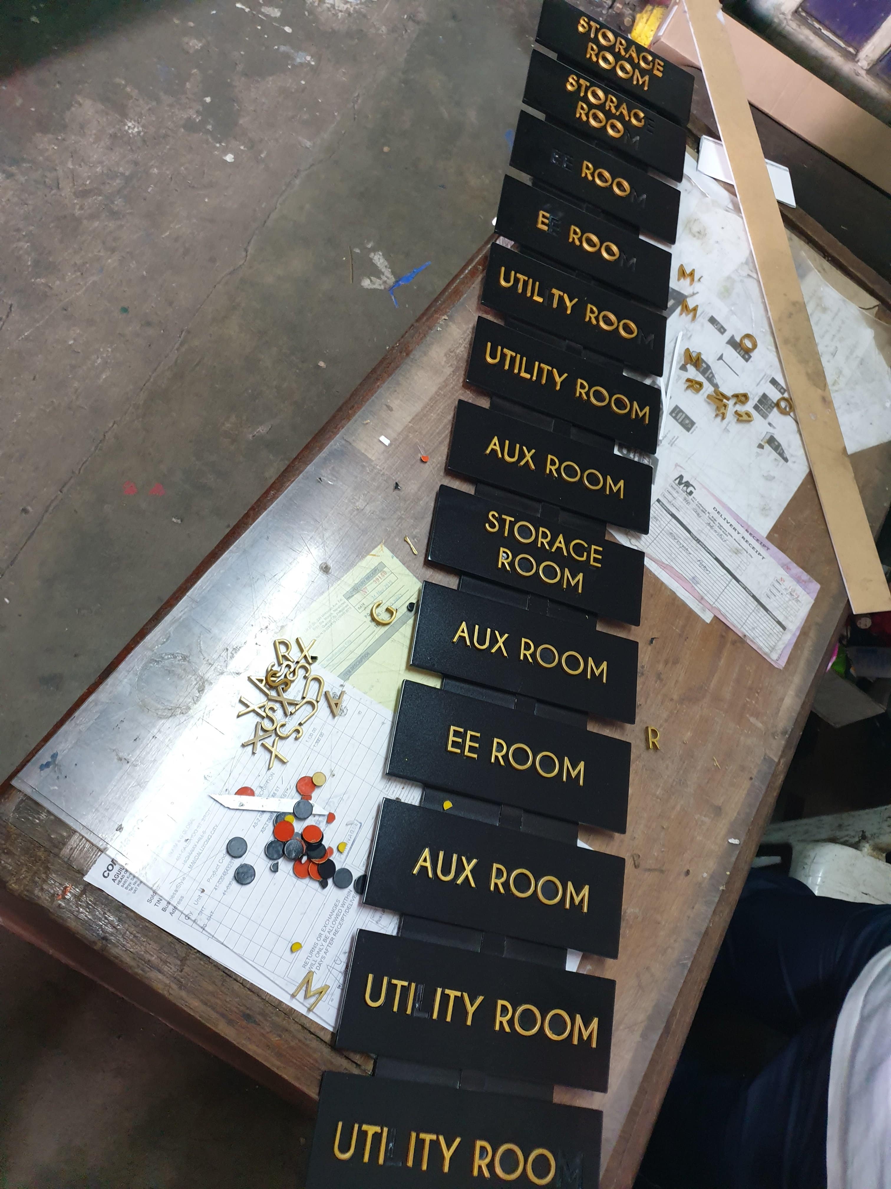Black acrylic office nameplates with gold lettering for building signage in Makati, installation tools visible by M&G Global Ads.