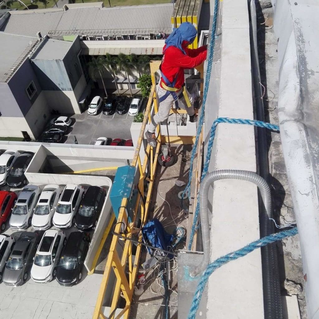 Installing acrylic signage on building facade in Ortigas, worker on scaffold above cars and buildings. By M&G Global Ads.