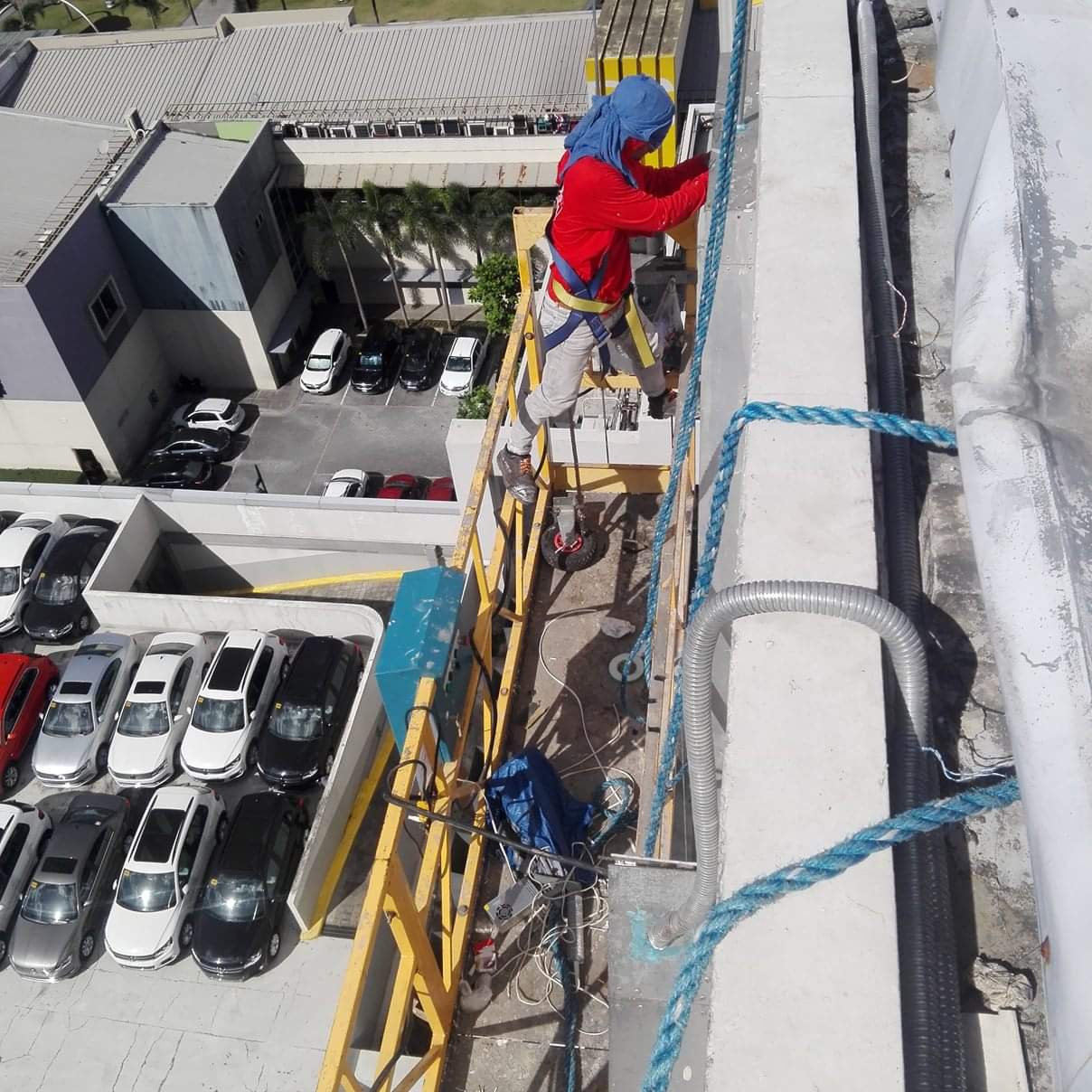 Installing acrylic signage on building facade in Ortigas, worker on scaffold above cars and buildings. By M&G Global Ads.